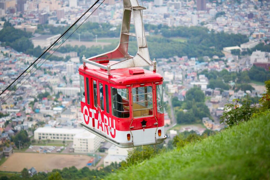 Vibrant red cable car ascending over Otaru with cityscape in view, Japan.